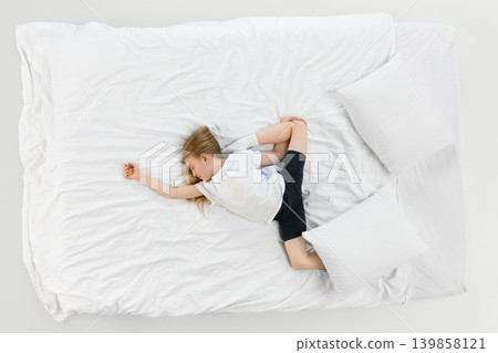 Little girl sleeping diagonally across white bed in airy minimalist bedroom. Little girl sleeping diagonally across white bed in airy minimalist bedroom. 139858121