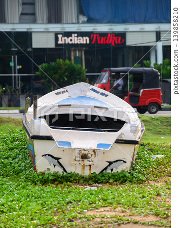 Abandoned fishing boat on urban coastal roadside with storefront background. 139858210