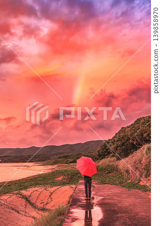 A sunset sky and rainbow appear at Hanarihama Park in Tanegashima, with a red umbrella in the background. A sunset sky and rainbow appear at Hanarihama Park in Tanegashima, with a red umbrella in the background. 139858970