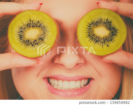 Woman holding green kiwi fruit like eyeglasses Woman holding green kiwi fruit like eyeglasses 139858982