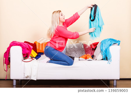 Woman looking through clothes on messy couch Woman looking through clothes on messy couch 139859003
