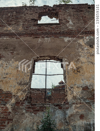 A weathered brick wall of an old ruined building stands. Two open windows show a cloudy sky A weathered brick wall of an old ruined building stands. Two open windows show a cloudy sky 139859181