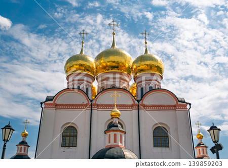 Majestic Assumption Cathedral at Valdai Iversky Monastery showcasing golden onion domes under a bright cloudy sky Majestic Assumption Cathedral at Valdai Iversky Monastery showcasing golden onion domes under a bright cloudy sky 139859203