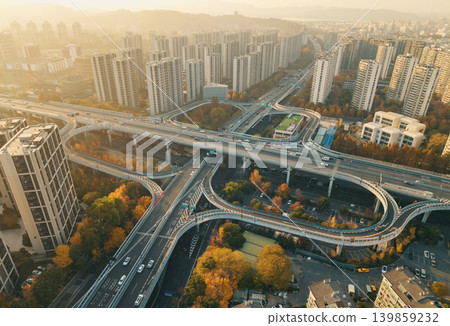 Cars move on a multi-level highway interchange cutting through a city filled with numerous tall residential and commercial structures 139859232