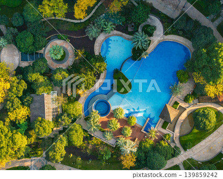 Expansive outdoor swimming pools with brilliant blue water wind through a meticulously landscaped garden Expansive outdoor swimming pools with brilliant blue water wind through a meticulously landscaped garden 139859242