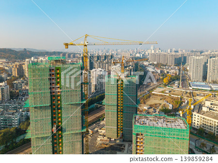 Aerial view of a bustling city showcasing ongoing construction of multiple high rise buildings covered with scaffolding netting and with large cranes operating Aerial view of a bustling city showcasing ongoing construction of multiple high rise buildings covered with scaffolding netting and with large cranes operating 139859284