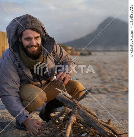 Portrait, smile and man at beach with campfire on holiday, vacation or travel toe prepare for winter outdoor alone. Happy person, wood and adventure at seashore, leisure and recreation in Canada Portrait, smile and man at beach with campfire on holiday, vacation or travel toe prepare for winter outdoor alone. Happy person, wood and adventure at seashore, leisure and recreation in Canada 139859729