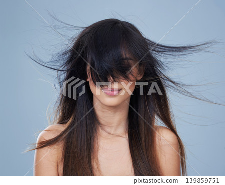 Studio, model and wind with long hair in eyes, mock up and keratin treatment for shine or salon result. Arab woman, beauty or relax with conditioner for haircare, health or shampoo by blue background Studio, model and wind with long hair in eyes, mock up and keratin treatment for shine or salon result. Arab woman, beauty or relax with conditioner for haircare, health or shampoo by blue background 139859751