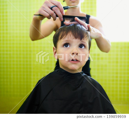 Child, boy and barber with haircut at salon for grooming, hairstyle or serious with scissors. Hairdresser, person or kid for hair treatment, haircare and hairdressing with comb, confidence or looking Child, boy and barber with haircut at salon for grooming, hairstyle or serious with scissors. Hairdresser, person or kid for hair treatment, haircare and hairdressing with comb, confidence or looking 139859939
