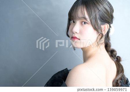 一位身穿黑色連身裙的日本女子在灰色背景下轉身。 一位身穿黑色連身裙的日本女子在灰色背景下轉身。 139859971