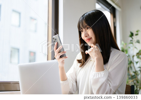 Japanese woman working in the office using a laptop and smartphone. Japanese woman working in the office using a laptop and smartphone. 139860033