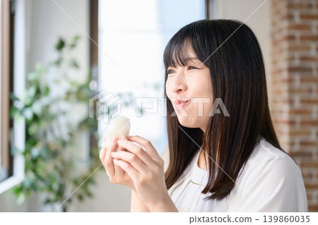 A Japanese woman eating a rice ball during her lunch break at the office. 139860035
