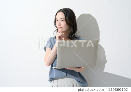 一位日本女性手持筆記型電腦,表情憂慮,背景為白色。 一位日本女性手持筆記型電腦,表情憂慮,背景為白色。 139860102