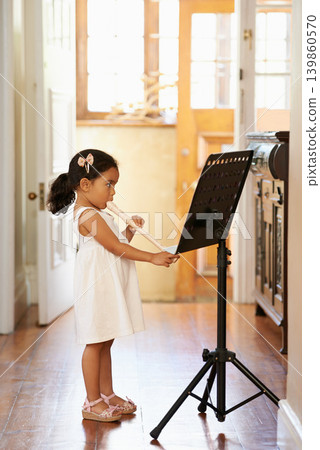 Flute, girl and child playing in home for learning, education and reading music sheet to practice performance. Art, flutist and kid with talent, creative or hobby with instrument for sound at lesson Flute, girl and child playing in home for learning, education and reading music sheet to practice performance. Art, flutist and kid with talent, creative or hobby with instrument for sound at lesson 139860570