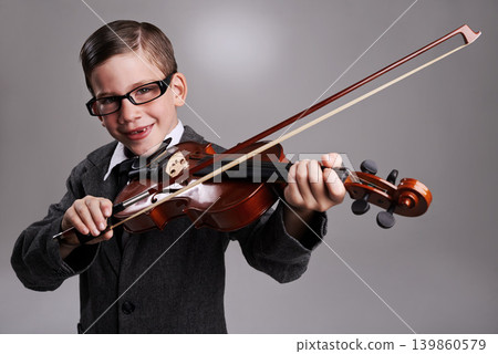 Smile, music and child with violin in studio for practice with suit and glasses for fashion. Happy, style and portrait of young boy kid play string instrument with spectacles by gray background. 139860579