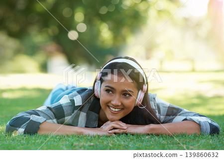 Woman, headphones and streaming music on grass, radio and internet for podcast in outdoors. Female person, happy and relaxing on lawn, weekend playlist and subscription for audio or sound on vacation 139860632