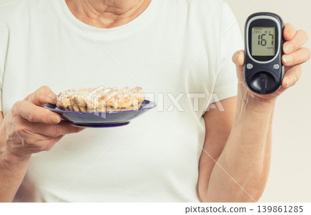 Senior woman holding fresh cake and glucometer with high result of sugar level. Diabetes in old age Senior woman holding fresh cake and glucometer with high result of sugar level. Diabetes in old age 139861285