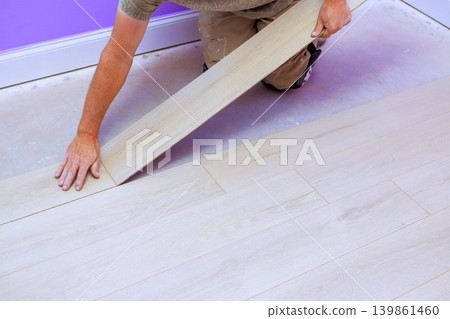 Handy worker places wooden floor board in room with purple walls while working on home improvement task. Handy worker places wooden floor board in room with purple walls while working on home improvement task. 139861460