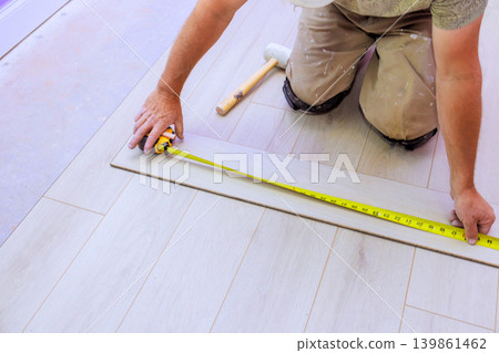 Carpenter is measuring tile on laminate floor to get right size for installation. Carpenter is measuring tile on laminate floor to get right size for installation. 139861462