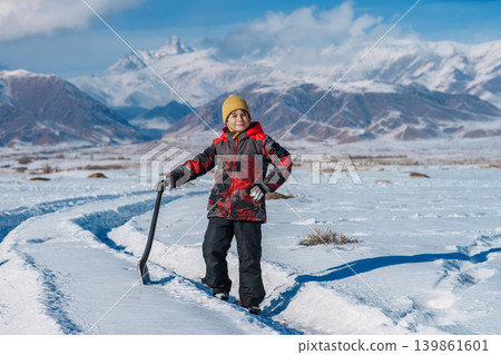 Child with shovel standing on winter mountains background Child with shovel standing on winter mountains background 139861601