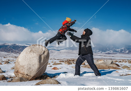 Child jumping on daddy from big wall on mountains background at winter season Child jumping on daddy from big wall on mountains background at winter season 139861607