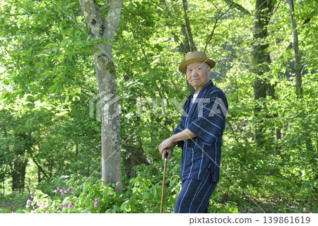 一位老人在綠樹環繞中拄著拐杖做復健運動。 一位老人在綠樹環繞中拄著拐杖做復健運動。 139861619