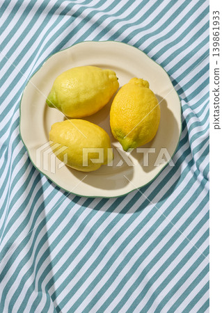 Fresh Lemons on a White Ceramic Plate on a Wrinkled Blue Striped Tablecloth. Top View Fresh Lemons on a White Ceramic Plate on a Wrinkled Blue Striped Tablecloth. Top View 139861933
