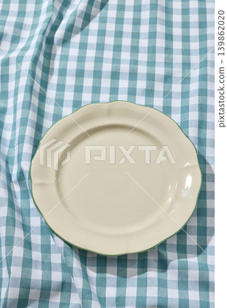 Empty White Ceramic Plate on a Wrinkled Blue Checked Tablecloth. Top View Empty White Ceramic Plate on a Wrinkled Blue Checked Tablecloth. Top View 139862020