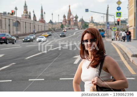 Woman in sunglasses smiles on Moscow street with Saint Basil Cathedral and city traffic in background, creating urban travel portrait in warm daylight. Tourism marketing, personal branding Woman in sunglasses smiles on Moscow street with Saint Basil Cathedral and city traffic in background, creating urban travel portrait in warm daylight. Tourism marketing, personal branding 139862396