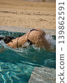 a girl with a beautiful tanned body having fun in the swimming pool of a luxury villa, the girl's butt is visible from under the water, azure water, splashes of water glow in the sun 139862591