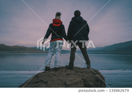 Man and woman holding hands on frozen lake background, dark retro style colors Man and woman holding hands on frozen lake background, dark retro style colors 139862679