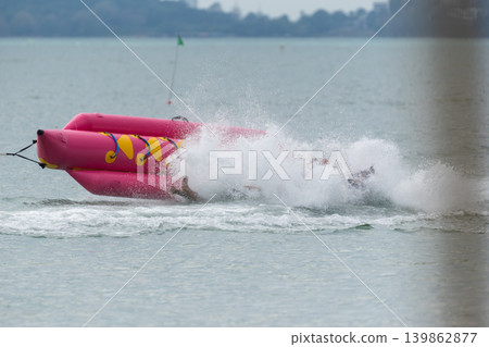 Tourists falling from banana boat during water sport ride creating dramatic splash exciting outdoor adventure activity Tourists falling from banana boat during water sport ride creating dramatic splash exciting outdoor adventure activity 139862877