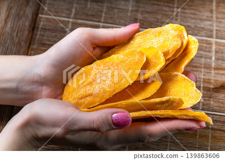 Young woman holding in hands dried mango on table background 139863606