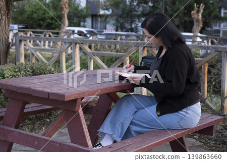 Female Working with Pen and Notebook Outdoors in Park. Female Working with Pen and Notebook Outdoors in Park. 139863660