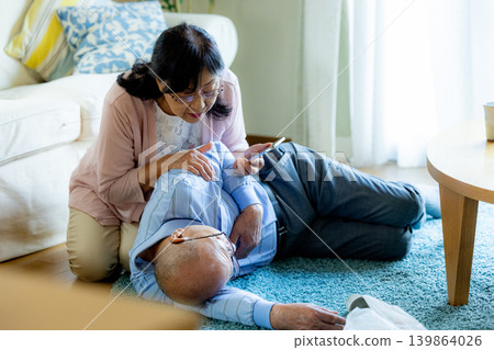 A senior man who has collapsed and a senior woman providing first aid. 139864026