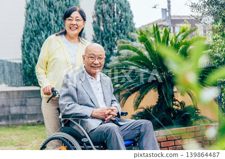 Wife supporting elderly person in wheelchair Wife supporting elderly person in wheelchair 139864487