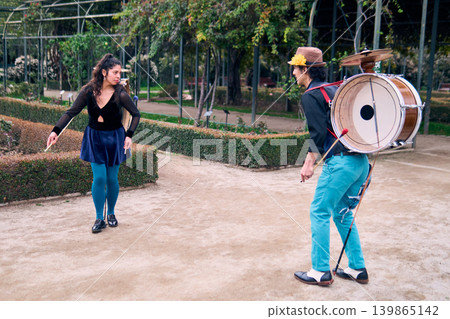 Couple of urban dancers, happily playing and dancing the cueca with a bass drum on their backs outdoors, Chilean chinchineros, street musicians who play the bass drum and dance in the streets Couple of urban dancers, happily playing and dancing the cueca with a bass drum on their backs outdoors, Chilean chinchineros, street musicians who play the bass drum and dance in the streets 139865142
