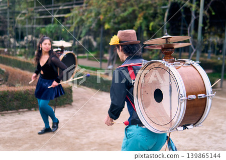 Couple of urban dancers, happily playing and dancing the cueca with a bass drum on their backs outdoors, Chilean chinchineros, street musicians who play the bass drum and dance in the streets Couple of urban dancers, happily playing and dancing the cueca with a bass drum on their backs outdoors, Chilean chinchineros, street musicians who play the bass drum and dance in the streets 139865144