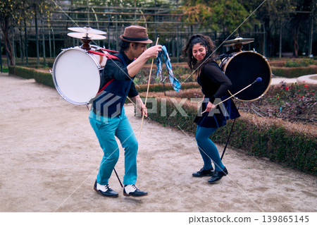 Couple of urban dancers, happily playing and dancing the cueca with a bass drum on their backs outdoors, Chilean chinchineros, street musicians who play the bass drum and dance in the streets 139865145