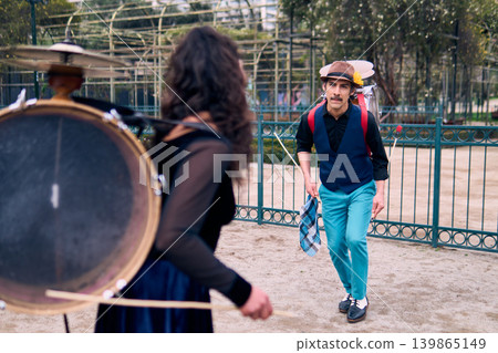 Adult couple of urban dancers, happily playing and dancing the cueca with a bass drum on their backs outdoors, Chilean chinchineros, street musicians who play the bass drum and dance in the streets 139865149