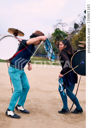 Adult couple of urban dancers, happily playing and dancing the cueca with a bass drum on their backs outdoors, Chilean chinchineros, street musicians who play the bass drum and dance in the streets Adult couple of urban dancers, happily playing and dancing the cueca with a bass drum on their backs outdoors, Chilean chinchineros, street musicians who play the bass drum and dance in the streets 139865165