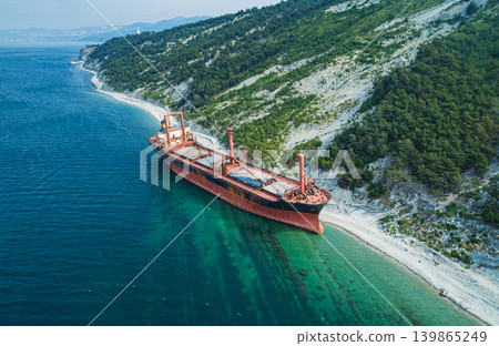 Stranded bulk carrier resting on a rocky shore beside a vibrant green forested hillside during daytime Stranded bulk carrier resting on a rocky shore beside a vibrant green forested hillside during daytime 139865249