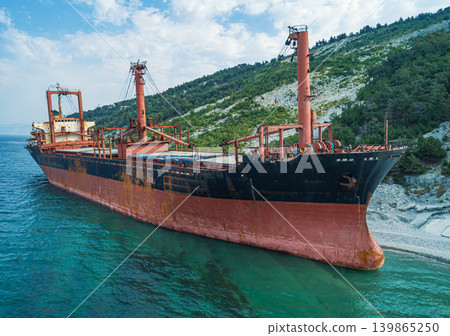 Grounded derelict cargo ship on a rocky Black Sea beach with green mountains under a bright sky Grounded derelict cargo ship on a rocky Black Sea beach with green mountains under a bright sky 139865250