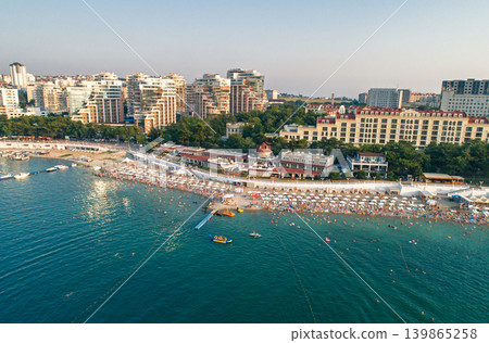 Aerial view captures hundreds of people enjoy a bustling resort city of Gelendzhik beach on a sunny summer day Aerial view captures hundreds of people enjoy a bustling resort city of Gelendzhik beach on a sunny summer day 139865258