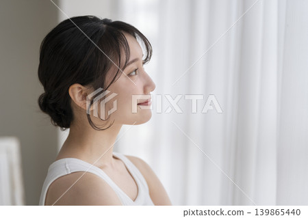 一位年輕女子在窗邊微笑，側臉。 139865440