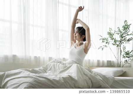 一位年輕女子醒來後在床上伸了個懶腰。 139865510