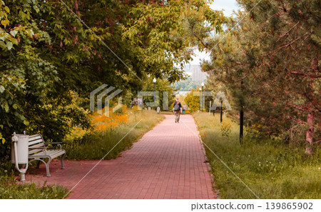 A path for walking in a city park with sunlight and shadows. Silhouette of an unrecognizable passerby, view from the back A path for walking in a city park with sunlight and shadows. Silhouette of an unrecognizable passerby, view from the back 139865902