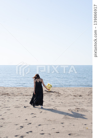 一名手捧鮮花的女子走在石川縣加賀市片野海岸的沙灘上(從背後拍攝)。 一名手捧鮮花的女子走在石川縣加賀市片野海岸的沙灘上(從背後拍攝)。 139866917