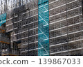 A high-rise construction site covered with scaffolding and protective netting. 139867033