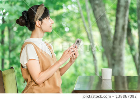 A woman's hands as she operates her smartphone in a cafe overlooking a lush green forest. 139867092